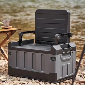 Könnte beinhalten: Ein grauer und schwarzer Klappstuhl und Aufbewahrungsbehälter. Der Stuhl hat eine Rückenlehne und Armlehnen, die sich von der Oberseite des Behälters ausklappen lassen. Der Behälter hat einen Griff und steht auf einem Steinhaufen.