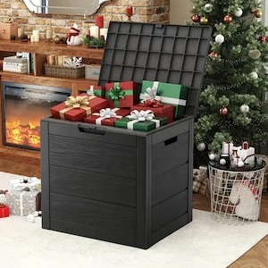 May include: A black storage chest with an open lid, filled with wrapped gifts in red and green. The chest has a wood-grain texture and is placed near a Christmas tree and fireplace, suggesting a holiday theme.