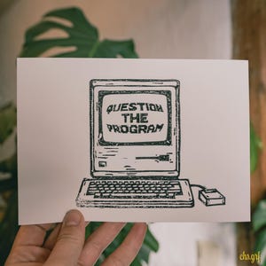 Könnte beinhalten: Schwarz-Weiß-Illustration eines Vintage-Computers mit dem Text "QUESTION THE PROGRAM" auf dem Bildschirm. Das Bild ist auf einer cremefarbenen Karte gedruckt, die von einer Hand gehalten wird, mit einem grünen Hintergrund aus Blättern.