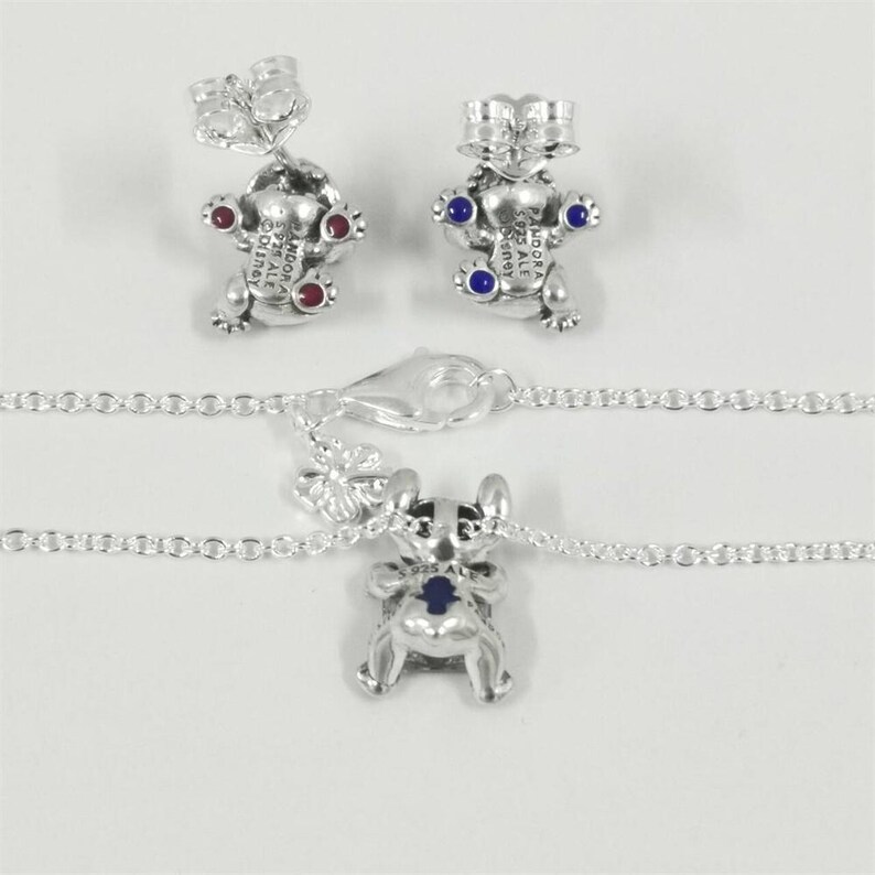 May include: Silver-coloured jewellery set featuring a charm necklace and matching stud earrings. The charms and earrings are shaped like a cartoon character with red and blue accents. The necklace has a delicate chain and a lobster clasp.