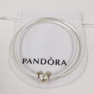 May include: A silver Pandora bracelet with a Mickey Mouse charm. The bracelet is a double strand design with a textured, snake chain pattern. The charm is a silver sphere with two small, round silver ears. The bracelet is on a white pouch with the Pandora logo.