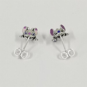 Pu&ograve; includere: Un paio di orecchini a bottone color argento con un design a personaggio dei cartoni animati. Gli orecchini raffigurano una piccola creatura stilizzata con orecchie viola, occhi blu e un'espressione sorridente. Gli orecchini hanno una chiusura a farfalla.