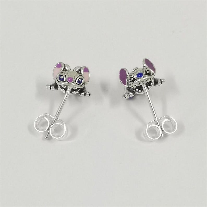 Pu&ograve; includere: Un paio di orecchini a bottone color argento con un design a personaggio dei cartoni animati. Gli orecchini raffigurano una piccola creatura stilizzata con orecchie viola, occhi blu e un'espressione sorridente. Gli orecchini hanno una chiusura a farfalla.