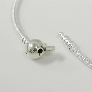 May include: A silver bracelet with a Mickey Mouse-shaped clasp. The clasp is detailed with the word "Disney" and a small black circle. The bracelet is unclasped, showing the two ends of the chain.