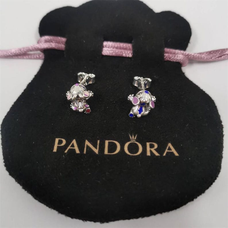 Pu&ograve; includere: Orecchini a lobo in argento con un design a personaggio dei cartoni animati, con dettagli in smalto rosa, viola e blu. Gli orecchini sono esposti su un sacchetto di velluto nero con il logo "PANDORA".