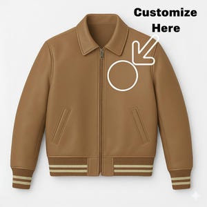 Pode incluir: Casaco de couro castanho com gola, fecho de correr e dois bolsos frontais. O casaco tem punhos e bainha canelados com riscas bege. O texto "Customize Here" está acima de um círculo e um gráfico de seta.