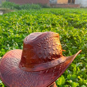 Peut inclure: Un chapeau de cowboy marron dot&eacute; d'un motif textur&eacute; en relief imitant l'apparence de la peau de reptile. Le chapeau pr&eacute;sente une calotte structur&eacute;e et un large bord incurv&eacute;, avec une bande assortie entourant la base de la calotte.