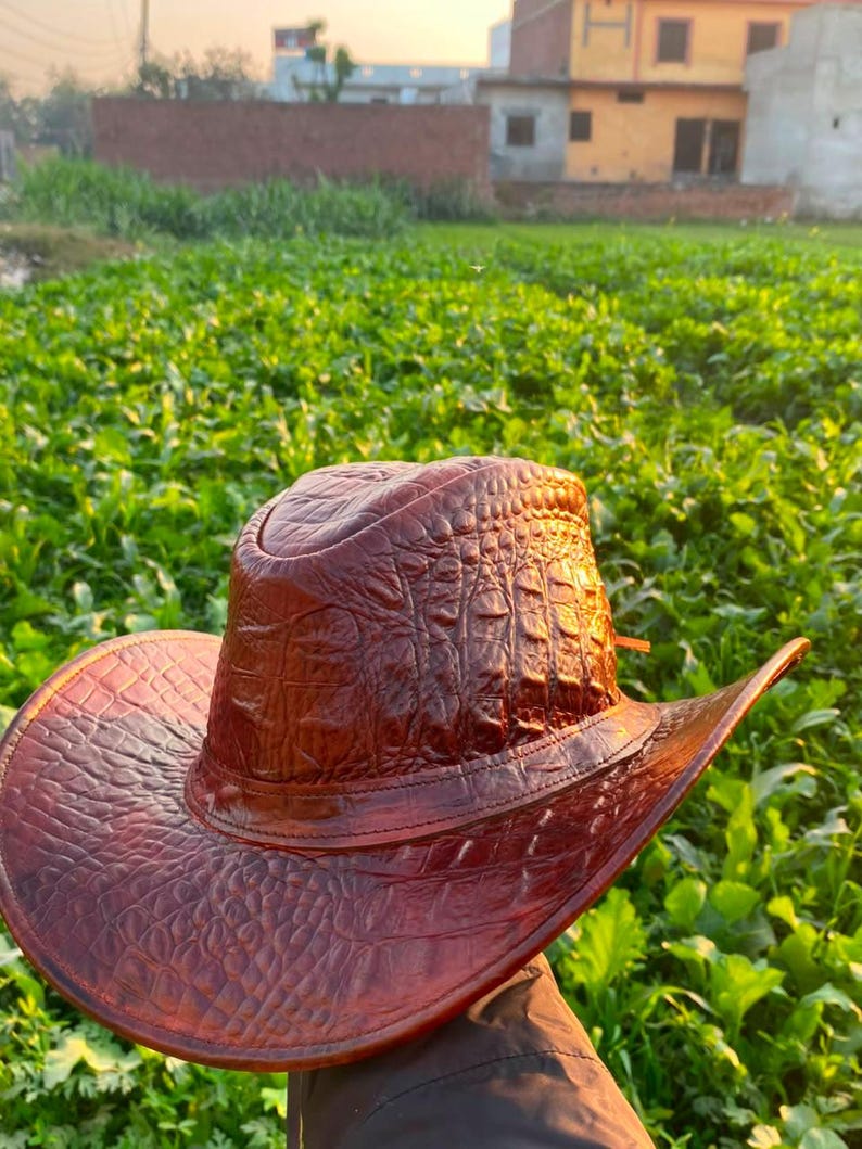 Peut inclure: Un chapeau de cowboy marron dot&eacute; d'un motif textur&eacute; en relief imitant l'apparence de la peau de reptile. Le chapeau pr&eacute;sente une calotte structur&eacute;e et un large bord incurv&eacute;, avec une bande assortie entourant la base de la calotte.