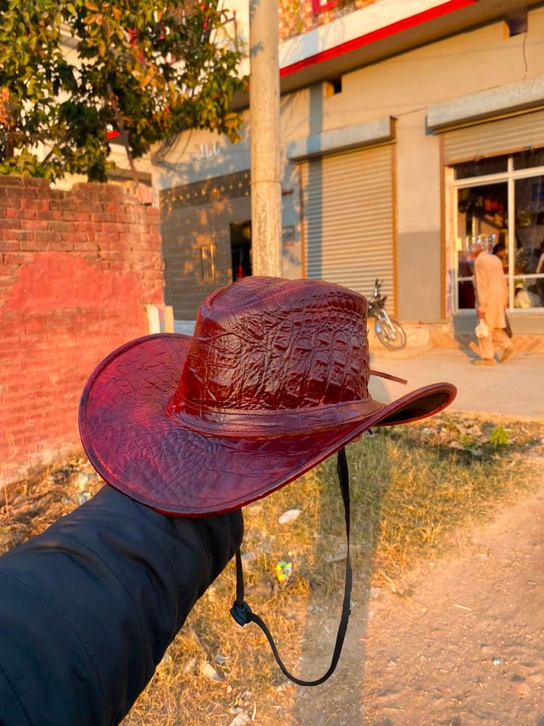 Peut inclure: Un chapeau de cowboy rouge fonc&eacute; pr&eacute;sentant un motif textur&eacute; en relief fa&ccedil;on peau de crocodile sur la calotte et les larges bords. Le chapeau comprend une fine jugulaire noire r&eacute;glable fix&eacute;e sur les c&ocirc;t&eacute;s pour maintenir le couvre-chef.