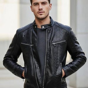 May include: Black leather jacket with a snakeskin pattern. The jacket has a stand-up collar, zippered pockets, and a front zipper closure. The model is wearing a gray shirt underneath.