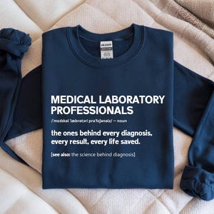 May include: A navy blue sweatshirt with white text that reads "MEDICAL LABORATORY PROFESSIONALS" and a definition. The text also states "the ones behind every diagnosis, every result, every life saved."