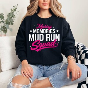 Puede incluir: Sudadera negra de cuello redondo con el texto "Making Memories Mud Run Squad" en blanco y rosa. La sudadera presenta un diseño casual, perfecta para un evento de carrera de barro o para uso diario.