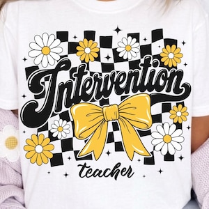 May include: A white t-shirt featuring a graphic design with a black and white checkered background, yellow daisies, and a large yellow bow. The text "Intervention" is written in a bold black script font above the bow, and "teacher" is below.