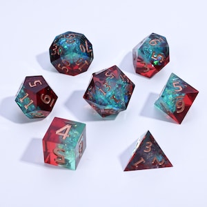 May include: Set of seven polyhedral dice in red and teal resin with gold numbering. The dice are in various geometric shapes, including a d20, d12, d10, d8, d6, and d4, perfect for tabletop gaming.