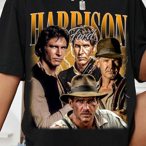 May include: Black t-shirt featuring a graphic of Harrison Ford in various roles, with the name "HARRISON FORD" in a yellow and orange vintage font. The design includes images of Ford from different movies.