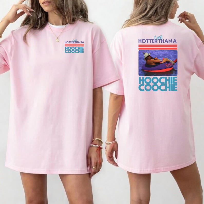 May include: Light pink t-shirt with the text "HOTTERTHANA HOOCHIE COOCHIE" on the front. The back of the shirt features a graphic of a person in a tube on the water, with the text "It gets HOTTERTHANA HOOCHIE COOCHIE".