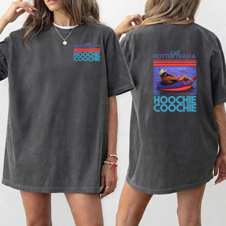 May include: Dark grey t-shirt with the text "A gets HOTTERTHANA HOOCHIE COOCHIE" on the front and a graphic on the back of a person floating in a tube. The graphic has a retro sunset design.