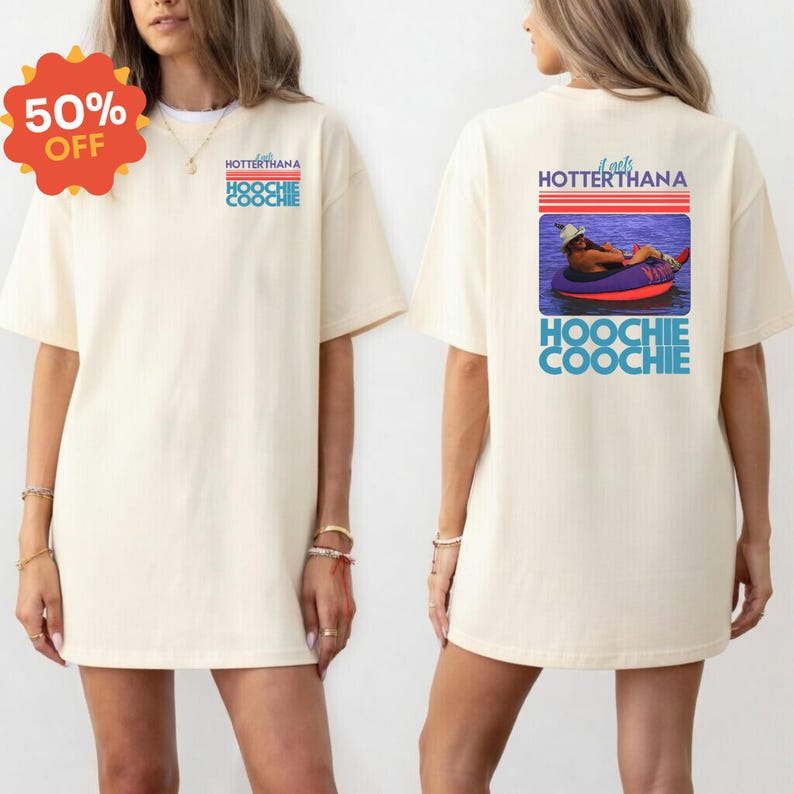 May include: Cream-colored t-shirt with the text "HOTTERTHANA HOOCHIE COOCHIE" on the front and a graphic on the back. The back graphic shows a person in a tube on the water. A 50% off sticker is on the top left.
