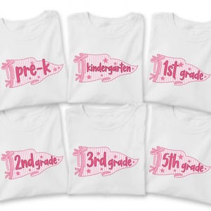 Könnte beinhalten: Sechs weiße T-Shirts mit rosa Wimpel-Grafiken, Streifenmustern und Sternen. Jedes T-Shirt zeigt eine andere Klassenstufe in rosa Schreibschrift: pre-k, kindergarten, 1st grade, 2nd grade, 3rd grade und 5th grade.