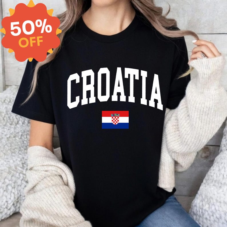 K&ouml;nnte beinhalten: Ein schwarzes Kurzarm-T-Shirt mit dem Wort CROATIA in gro&szlig;en, wei&szlig;en Gro&szlig;buchstaben, die bogenf&ouml;rmig &uuml;ber der Brust angeordnet sind, &uuml;ber einer kleinen rechteckigen Grafik der kroatischen Nationalflagge mit ihren roten, wei&szlig;en und blauen Querstreifen.
