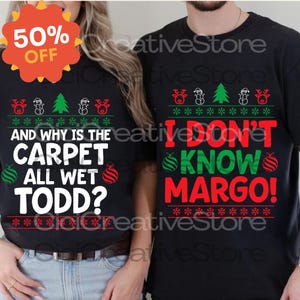 Puede incluir: Camisetas negras con temática navideña con diseños festivos y texto. Una camiseta dice "AND WHY IS THE CARPET ALL WET TODD?" y la otra dice "I DON'T KNOW MARGO!". Ambas camisetas tienen gráficos navideños.