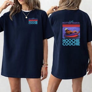 May include: Navy blue t-shirt with the text "HOTTERTHANA HOOCHIE COOCHIE" on the front and a graphic on the back of a person floating in a tube. The graphic includes the text "HOOCHIE COOCHIE".