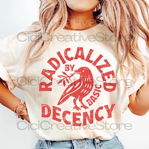 Könnte beinhalten: Cremefarbenes T-Shirt mit roter Grafik. Die Grafik zeigt einen Vogel, der einen Zweig in einem Kreis hält, mit den Worten "RADICALIZED BY BASIC DECENCY" in fetter, stilisierter Schrift. Das Shirt ist ein Freizeitartikel.