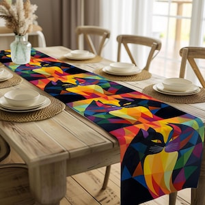 Puede incluir: Un colorido camino de mesa con un diseño geométrico de gatos negros con ojos amarillos. El camino de mesa presenta un patrón vibrante de triángulos en tonos de rojo, naranja, amarillo, verde, azul y morado. Se muestra sobre una mesa de madera.