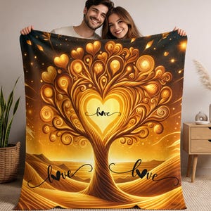 Può includere: Una coperta dorata con un albero stilizzato, un cuore centrale e la parola "love" in corsivo. Il design include foglie a forma di cuore e un paesaggio desertico. La coperta è tenuta da una coppia sorridente.