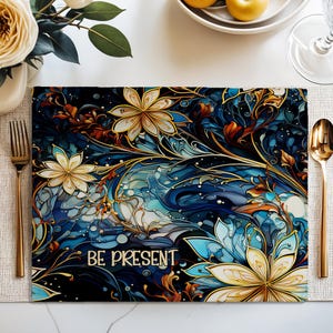 Può includere: Un sottopiatto rettangolare con un motivo floreale nei toni del blu, oro e bianco. Il sottopiatto presenta la scritta "BE PRESENT" in bianco. Sono visibili posate dorate e un vaso bianco con fiori.