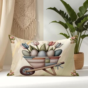 May include: A rectangular throw pillow featuring a central illustration of a wheelbarrow filled with pastel-colored eggs and tulips. The design uses a patchwork-style pattern in muted tones of blue, pink, and beige, accented by a small bow.