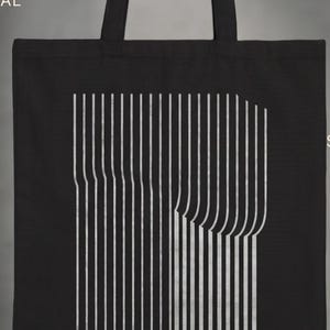 Może przedstawiać: Czarna torba typu tote z białym wzorem linii pionowych. Torba ma prostokątny kształt z uchwytem. Tekst "THE KINETIC TOTE" znajduje się na górze. Projekt opisano jako "Kinetic Line Art", "Architectural Feel", "Modern & Minimal" i "Graphic & Sophisticated".