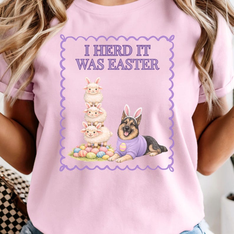 May include: Pink t-shirt with the text "I Herd It Was Easter" inside a purple scalloped border. The graphic features a stack of three sheep, a German Shepherd wearing bunny ears and a purple sweater, and a pile of Easter eggs.