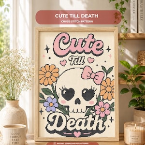 May include: A framed cross stitch pattern featuring a central white skull with heart-shaped eyes, a pink bow, and rosy cheeks. The text reads Cute Till Death in a bold font. The design is surrounded by orange, purple, and pink flowers and green leaves.