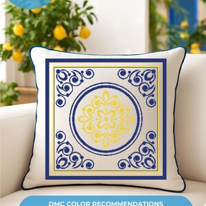 Op de afbeelding: Een vierkant kussen met een witte achtergrond, blauwe rand en een centraal ontwerp in geel en blauw. Het ontwerp bevat een cirkelvormig bloemmotief en decoratieve hoekelementen. Het kussen ligt op een witte bank. Tekst op de afbeelding zegt "DIGITAL PDF PATTERN + INSTANT DOWNLOAD".