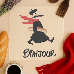 May include: Cross-stitch pattern with a French theme. The design features a figure carrying bread, wearing a beret and scarf, with the word "Bonjour" below. The image includes a baguette, coffee, and a red scarf.
