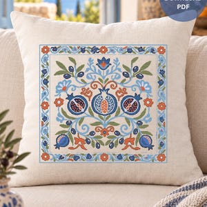 Puede incluir: Un cojín cuadrado de color beige con un patrón de punto de cruz centrado de granadas, hojas y flores en tonos azules, naranjas y verdes. El diseño está rodeado por un borde floral. Una insignia circular azul muestra INSTANT DOWNLOAD PDF.