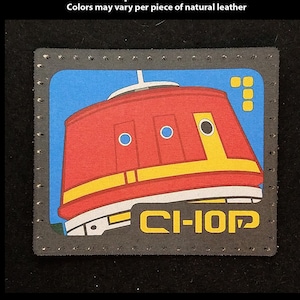 May include: A red, yellow, and black leather patch with a robot design and the text "CI-IOP". The patch is hand-printed and has a stitched border.