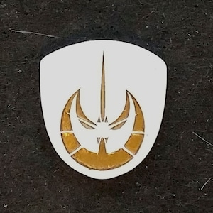 May include: A white shield with a gold symbol of a crescent moon and a sword. The symbol is similar to the symbol of the Mandalorian faction in Star Wars.