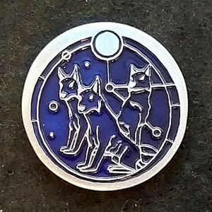 Pode incluir: Um broche circular prateado com fundo de esmalte azul. O broche apresenta um design estilizado de três gatos pretos com uma lua crescente e estrelas.