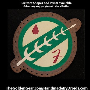 May include: A green, white, and red leather patch with a stylized symbol of a spear and a drop of blood. The patch is hand-stitched with brown thread and has a brown leather border. The text "7" is printed in red on the patch. The text "Hand Printed Leather Patches Custom Shapes and Prints available Colors may vary per piece of natural leather" is printed above the patch.