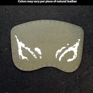May include: A gray leather patch with a white design of two abstract shapes. The patch is hand-printed and has a stitched edge. The text "Hand Printed Leather Patches" is at the top of the image. The text "Custom Shapes and Prints available" is below the first line of text. The text "Colors may vary per piece of natural leather" is below the second line of text. The text "TheGoldenGear.com/HandmadeByDroids.com" is at the bottom of the image.