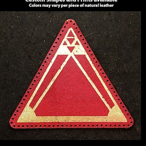 May include: A red leather patch in the shape of a triangle with a gold geometric design. The patch is hand-printed and has a dotted border.