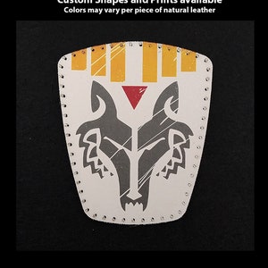 May include: A white leather patch with a gray wolf design and yellow and red accents. The patch is hand-stitched and has a distressed look. The text "Hand Printed Leather Patches" is at the top of the image. The text "Custom Shapes and Prints available" is below the first line of text. The text "Colors may vary per piece of natural leather" is below the second line of text. The text "TheGoldenGear.com/HandmadeByDroids.com" is at the bottom of the image.