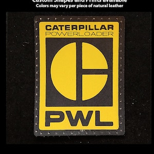 May include: A black and yellow leather patch with the text "Caterpillar Powerloader" and "PWL" in a black square with a dotted border.