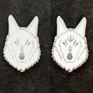 Pode incluir: Dois pinos de cabeça de lobo brancos com contorno detalhado. Os olhos do lobo estão fechados e o nariz é proeminente.