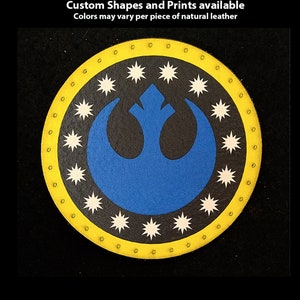 Peut inclure: Un patch en cuir rond de couleur jaune avec un symbole bleu de l'Alliance Rebelle et des étoiles blanches autour. Le texte "Hand Printed Leather Patches" est en haut de l'image. Le texte "Custom Shapes and Prints available" est en dessous de l'image. Le texte "Colors may vary per piece of natural leather" est en dessous de la deuxième ligne de texte.