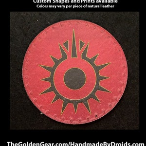 May include: A round, red leather patch with a black and gold sunburst design. The patch has a black circle in the center with a gold outline. The text "Hand Printed Leather Patches" is at the top of the image. The text "Custom Shapes and Prints available" is below the first line of text. The text "Colors may vary per piece of natural leather" is below the second line of text. The text "TheGoldenGear.com/HandmadeByDroids.com" is at the bottom of the image.