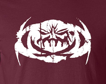 May include: A maroon t-shirt with a white graphic of a stylized face with a jagged, circular design around it.