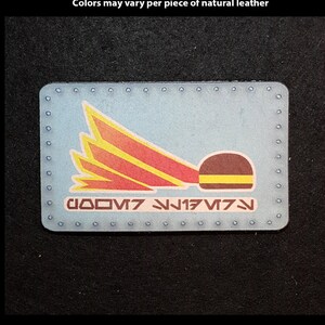 May include: A blue leather patch with a red and yellow rocket ship design and the text "000V7 177N".